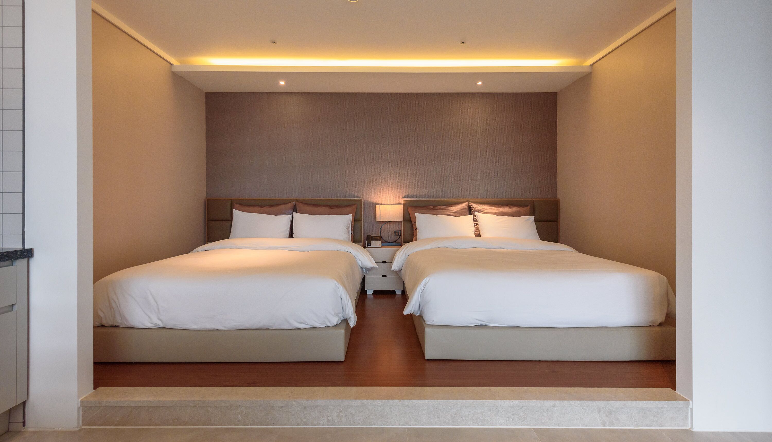 A hotel room with two beds, a nightstand with a lamp, and a small drawer.