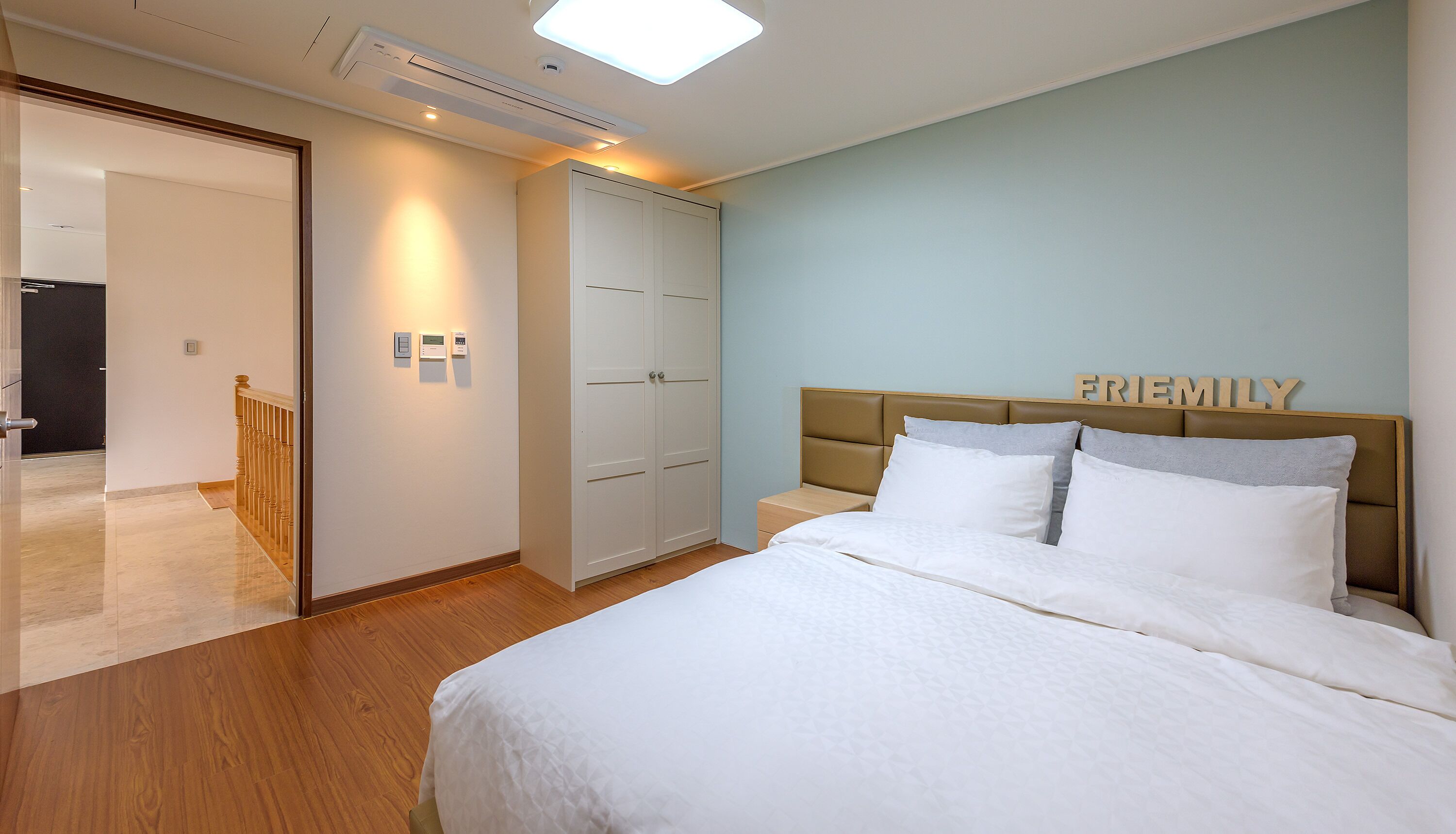 A bedroom with a bed, a wardrobe, a bedside table, and a wall-mounted thermostat.