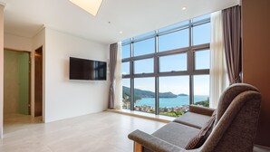 A spacious room with a large window offering a view of a coastal area, a flat-screen TV mounted on the wall, and a comfortable seating area with a sofa and armchair. - Friemily Pool Villa & Hotel (Geoje)