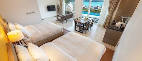 A hotel room with two beds, a dining area, and a view of the sea.
