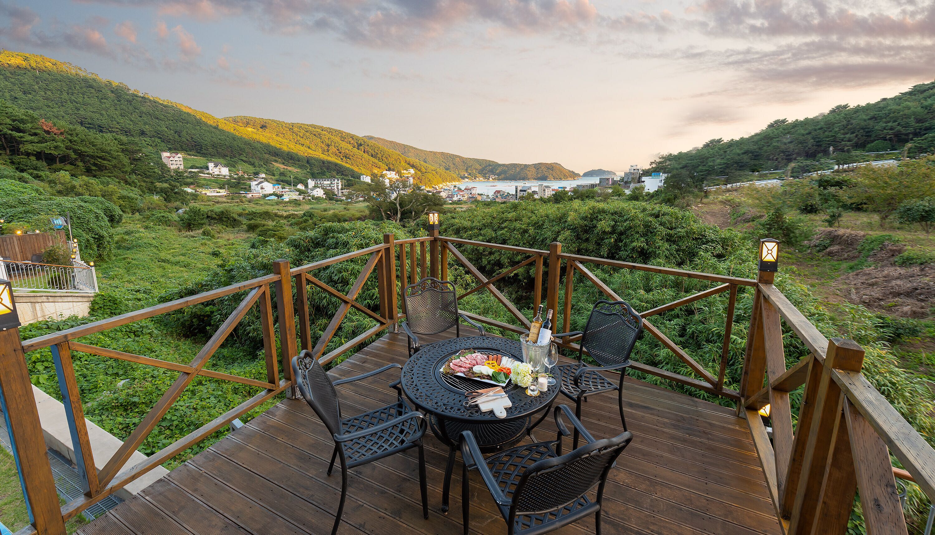 Eine Holzterrasse mit Tisch und Stühlen, mit Blick auf ein Tal mit Gebäuden und einem Gewässer.