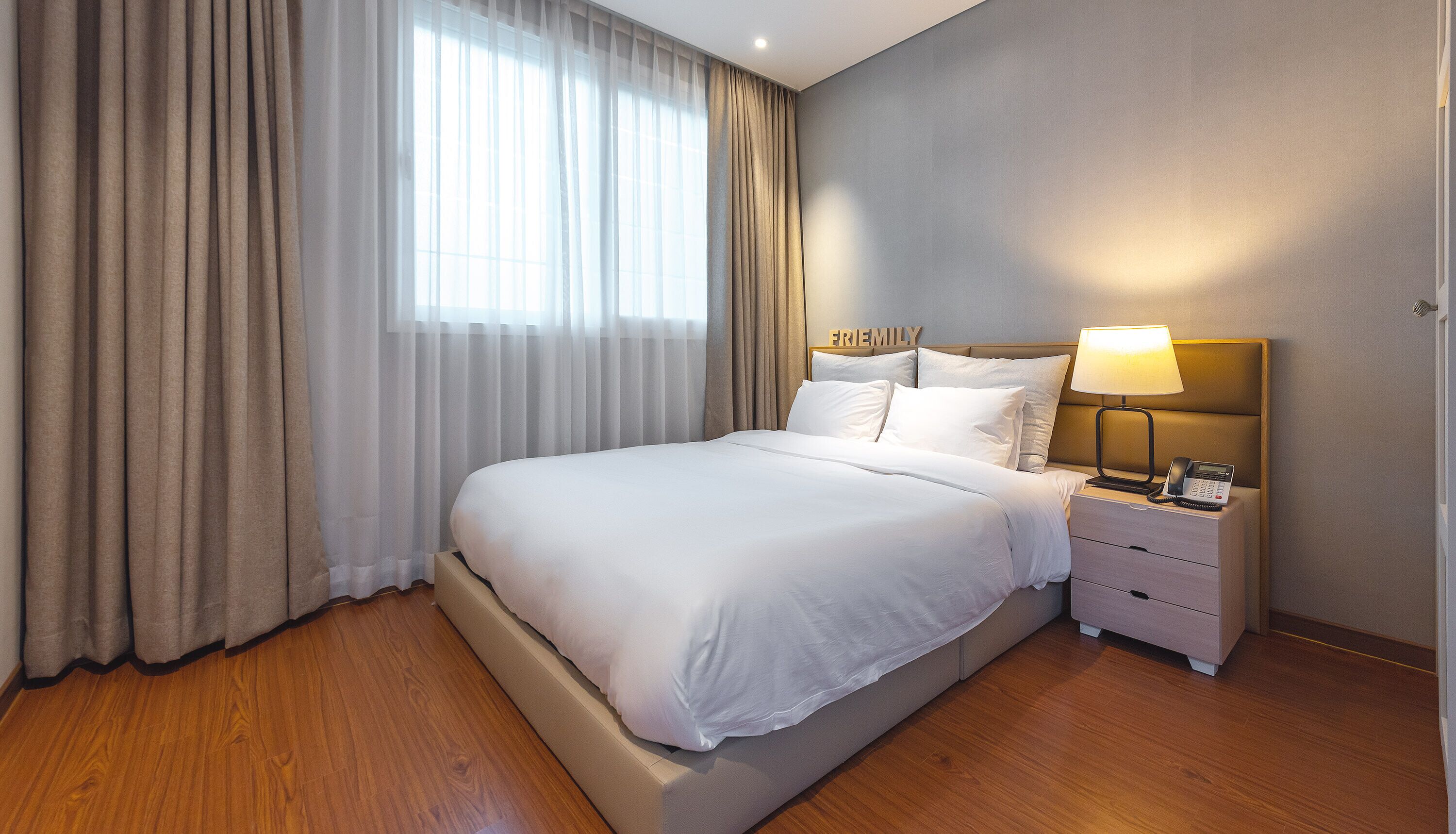 Une chambre d’hôtel avec un grand lit, une table de chevet avec une lampe et une fenêtre avec des rideaux.
