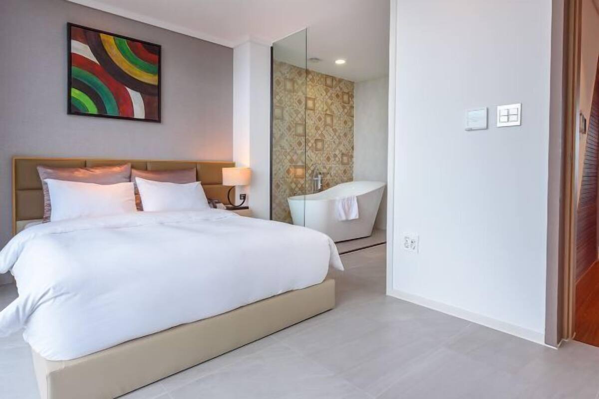 A hotel room with a bed, a bedside lamp, a bathroom with a bathtub, and a mirror.