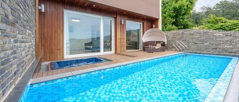 Een modern buitenzwembad met een houten terras, een ingebouwd whirlpool en een stenen muur.