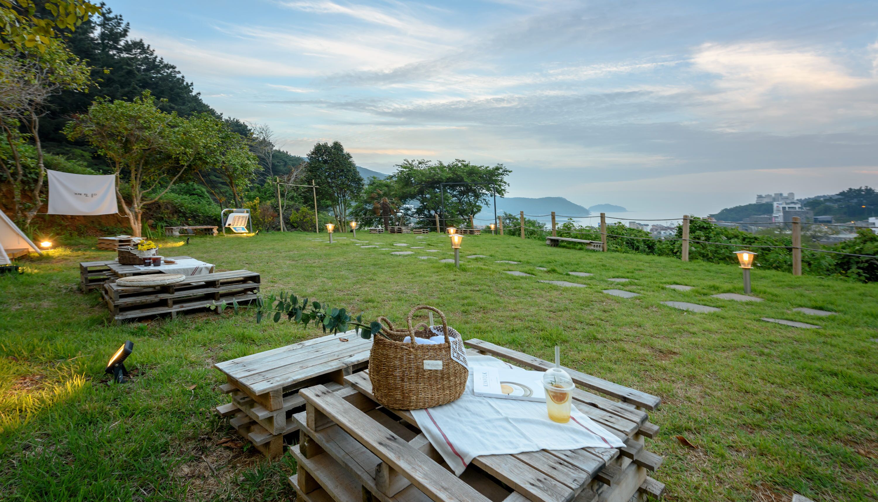 Un espace extérieur verdoyant avec des tables de pique-nique en bois, un panier en osier et une table sur laquelle se trouvent une boisson et un menu.
