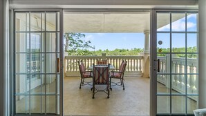 A covered patio with a table and chairs, a white balustrade, and a view of greenery.
