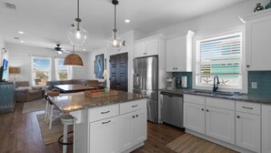 A modern kitchen with white cabinets, a stainless steel refrigerator, and a large island with a granite countertop. - Shellfish Cottage offers gulf views, pool, hot tub, outdoor kitchen! Steps to beach! (Port Saint Joe)
