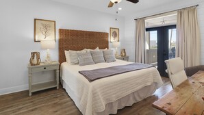 A bedroom with a large bed, a wooden headboard, two bedside tables with lamps, a ceiling fan, and a view through a sliding door. - Shellfish Cottage offers gulf views, pool, hot tub, outdoor kitchen! Steps to beach! (Port Saint Joe)