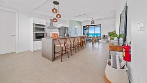 A modern kitchen with a central island, bar stools, and a fire extinguisher on the wall. - VIDA Cayman (West Bay)