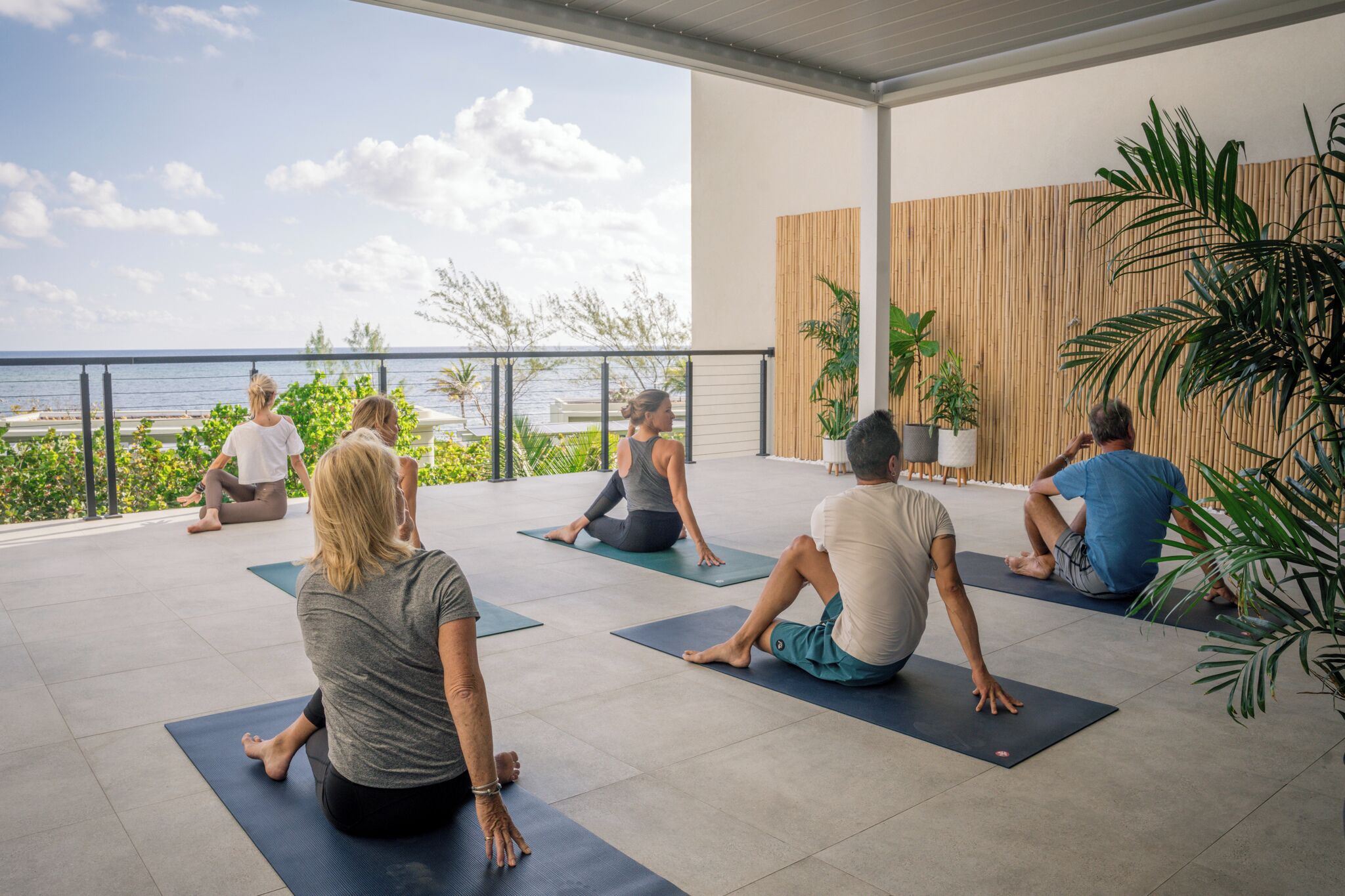 A group of people doing yoga on mats in an outdoor area with a view of the ocean.