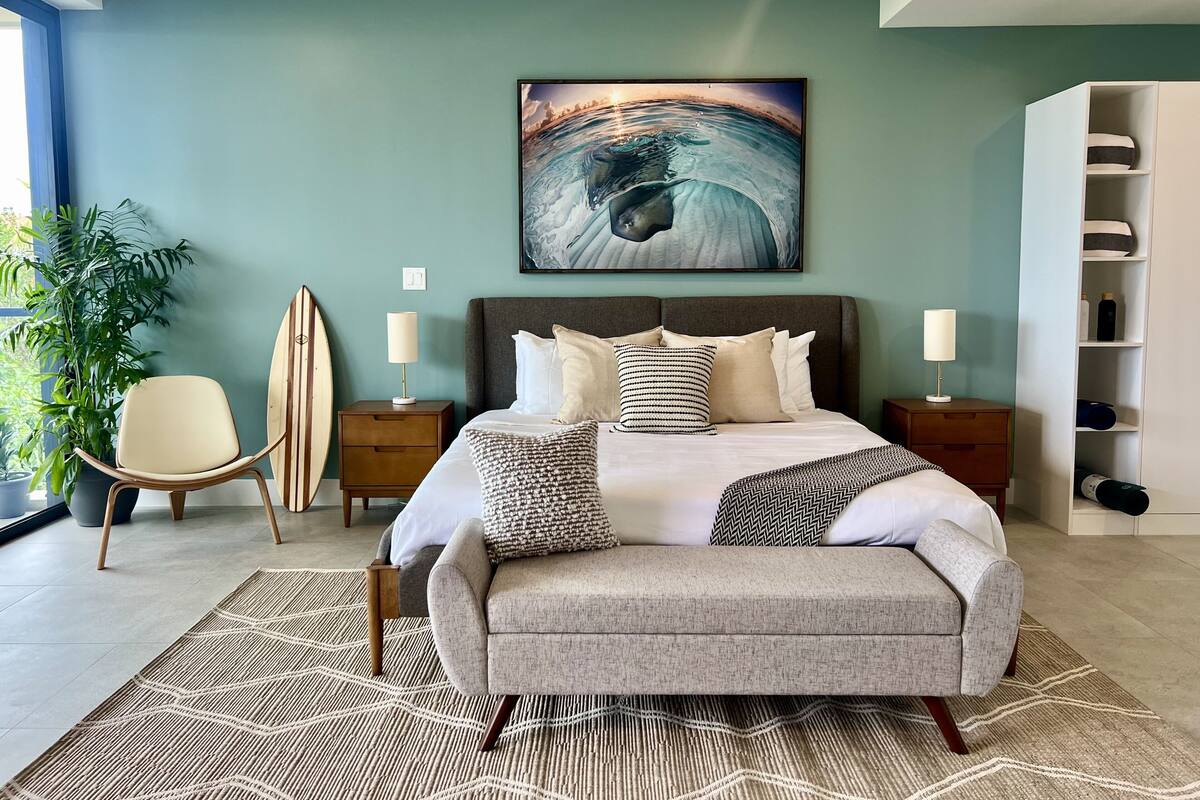Une chambre moderne avec un grand lit, une planche de surf, une chaise et une bibliothèque.