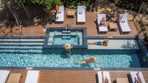 A pool area with lounge chairs, a hot tub, and a wooden deck. - VIDA Cayman (West Bay)