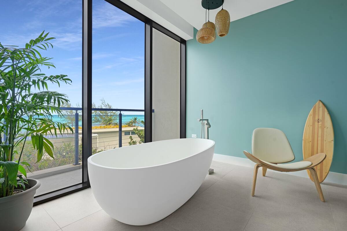 Une salle de bain moderne avec une baignoire sur pieds, une chaise et une planche de surf, le tout adossé à un mur de couleur turquoise.