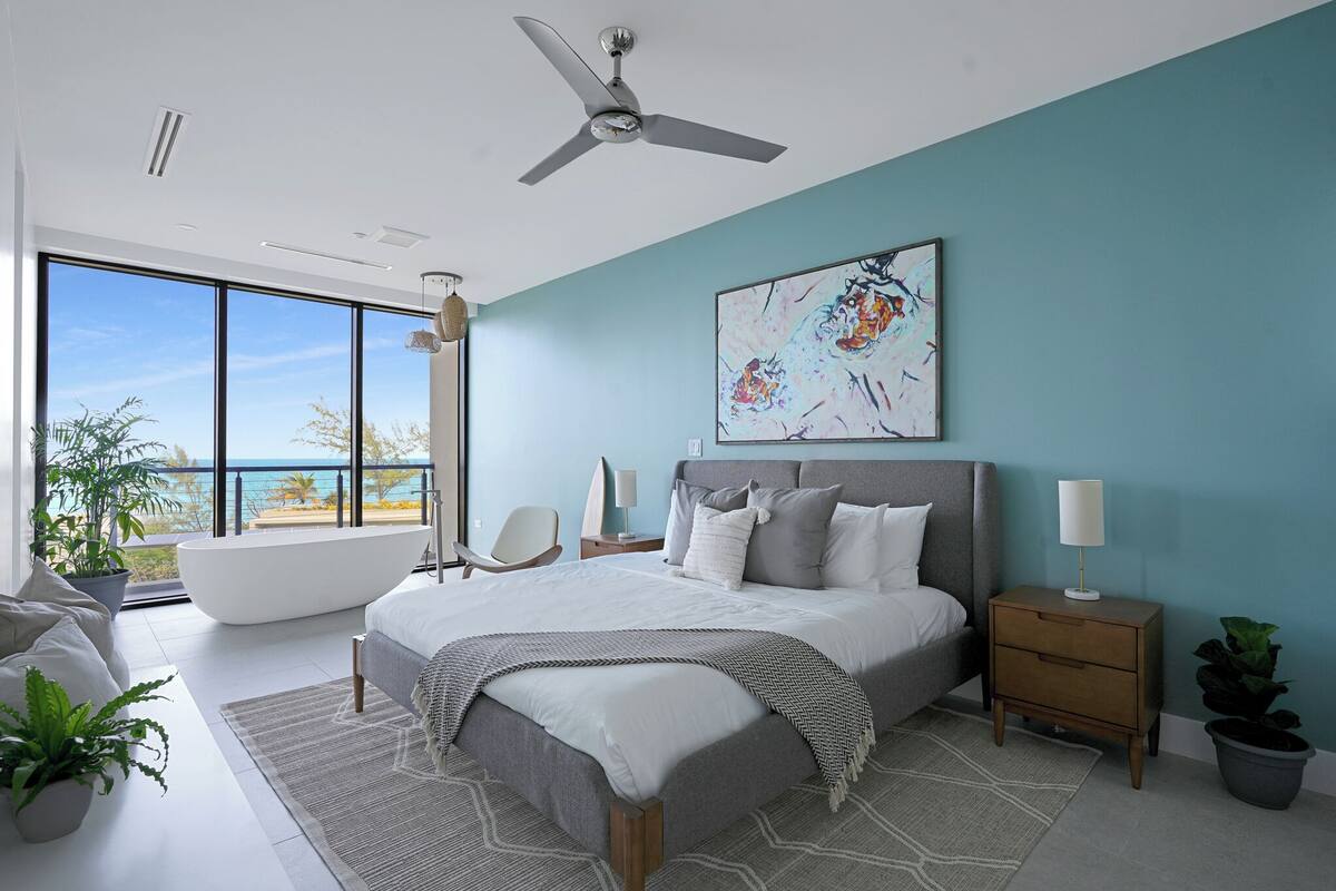 Une chambre moderne avec un grand lit, un ventilateur de plafond, une vue sur l’océan et une grande fenêtre.