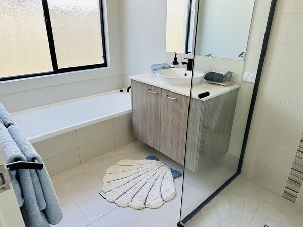 A modern bathroom with a bathtub, a sink, and a mirror. - Dunsborough, Spacious new 5 bedroom, 3 bathroom home (Dunsborough)
