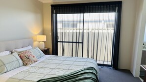 Une chambre d’hôtel avec un lit, une table de chevet avec une lampe, une vue sur l’extérieur par une fenêtre avec des rideaux et un sol recouvert de moquette.