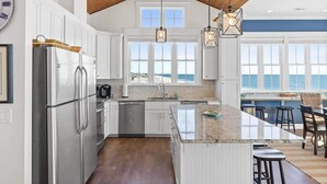 Une cuisine moderne dotée d’un grand îlot central, d’appareils électroménagers en acier inoxydable et offrant une vue sur la mer.
