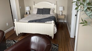 Ein Schlafzimmer mit einem Bett, zwei Nachttischen, einem Sessel, einer Pflanze und zwei Wandbildern.