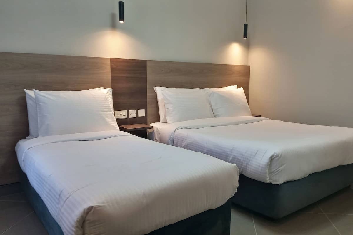 Une chambre d’hôtel avec deux lits simples, une tête de lit en bois, des tables de chevet et des lampes fixées au mur.