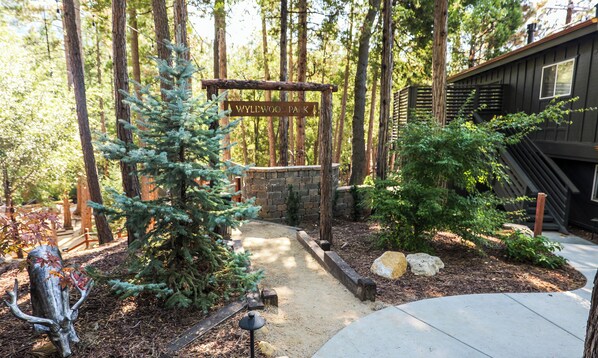 A sign for Wylwood Park, surrounded by a forest with a stone wall and a wooden deck.