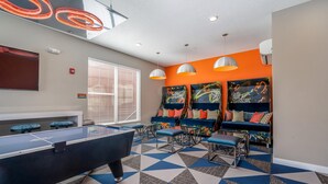 A pool table in a room with a geometric patterned floor, a sofa with colorful cushions, and a wall with abstract art.