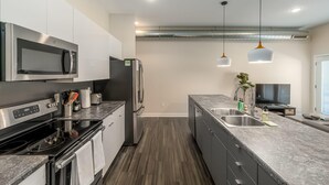A modern kitchen with stainless steel appliances, a marble countertop, and pendant lighting.