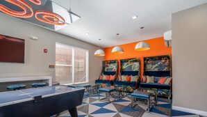 Ein Billardtisch in einem Raum mit geometrischem Fußboden, ein blaues Sofa mit bunten Kissen und eine Wand mit abstrakter Kunst.