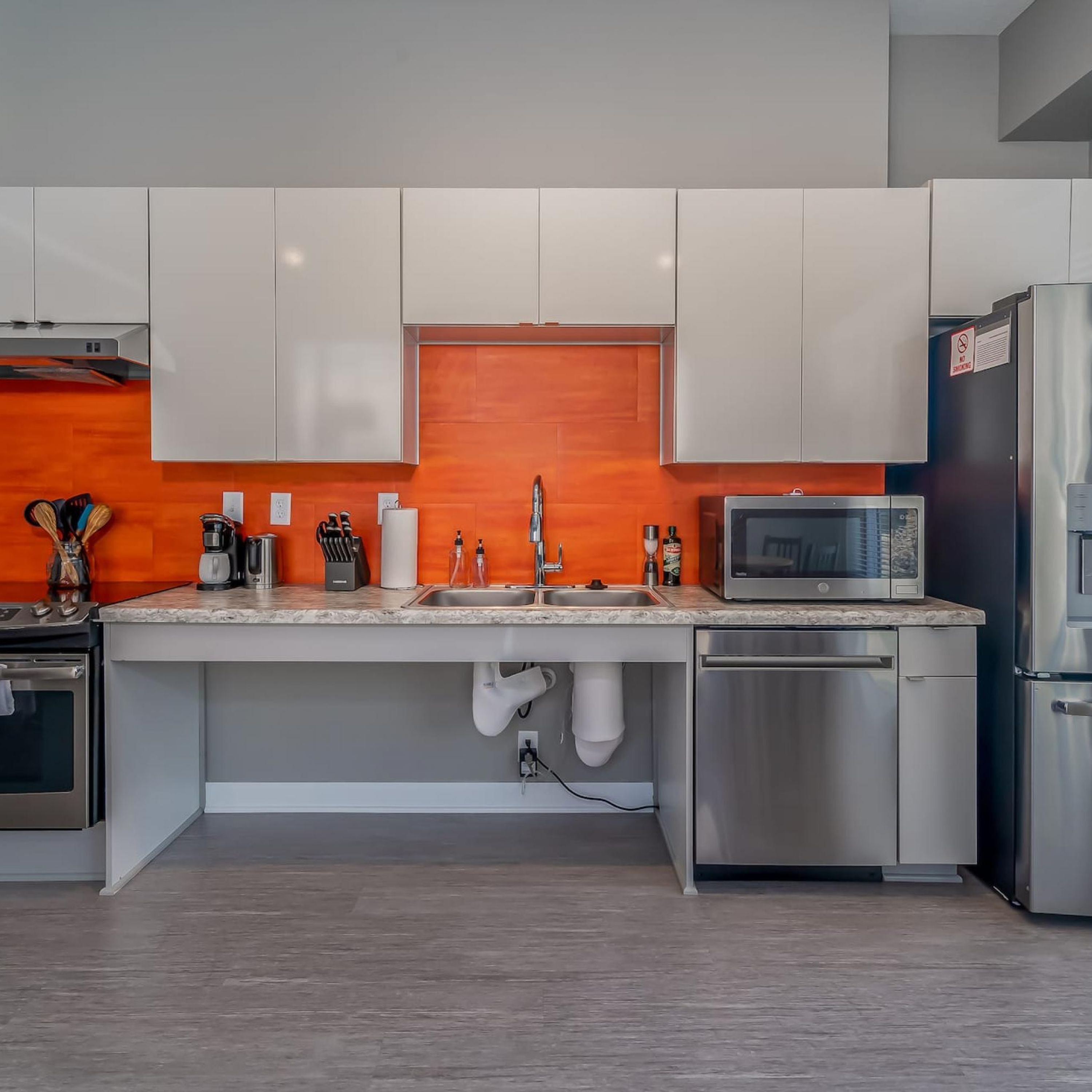 A modern kitchen with white cabinets, a stainless steel refrigerator, a microwave, and a sink with a faucet.