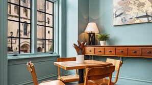 A room with a wooden table and chairs, a lamp, a potted plant, and a view of a building through a window. - Kasa Accessible Studio in the Heart of Steel City The Maverick (Pittsburgh)