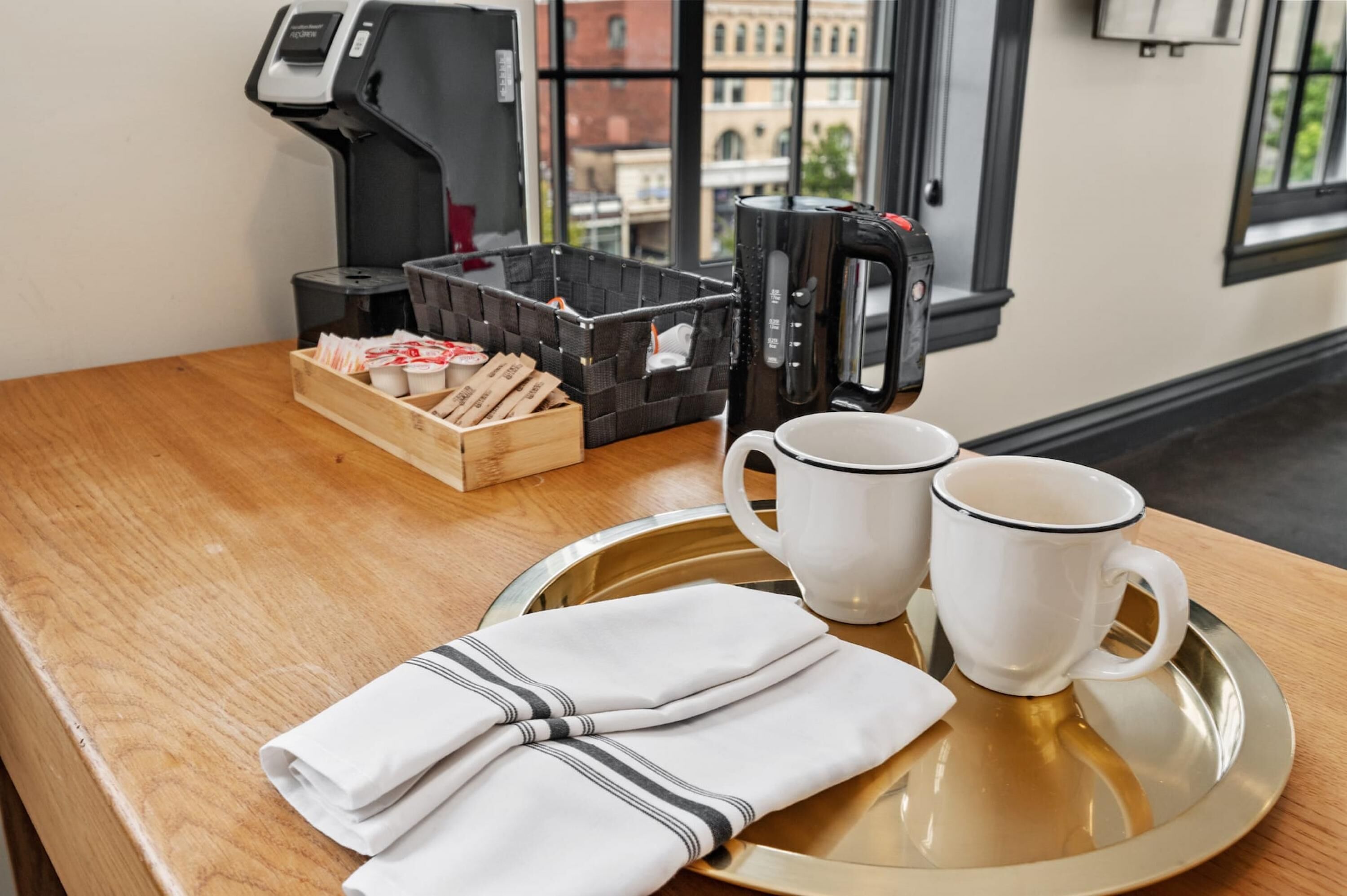 Un plateau de petit-déjeuner avec deux tasses blanches, une serviette pliée et une cafetière, le tout posé sur une table en bois.