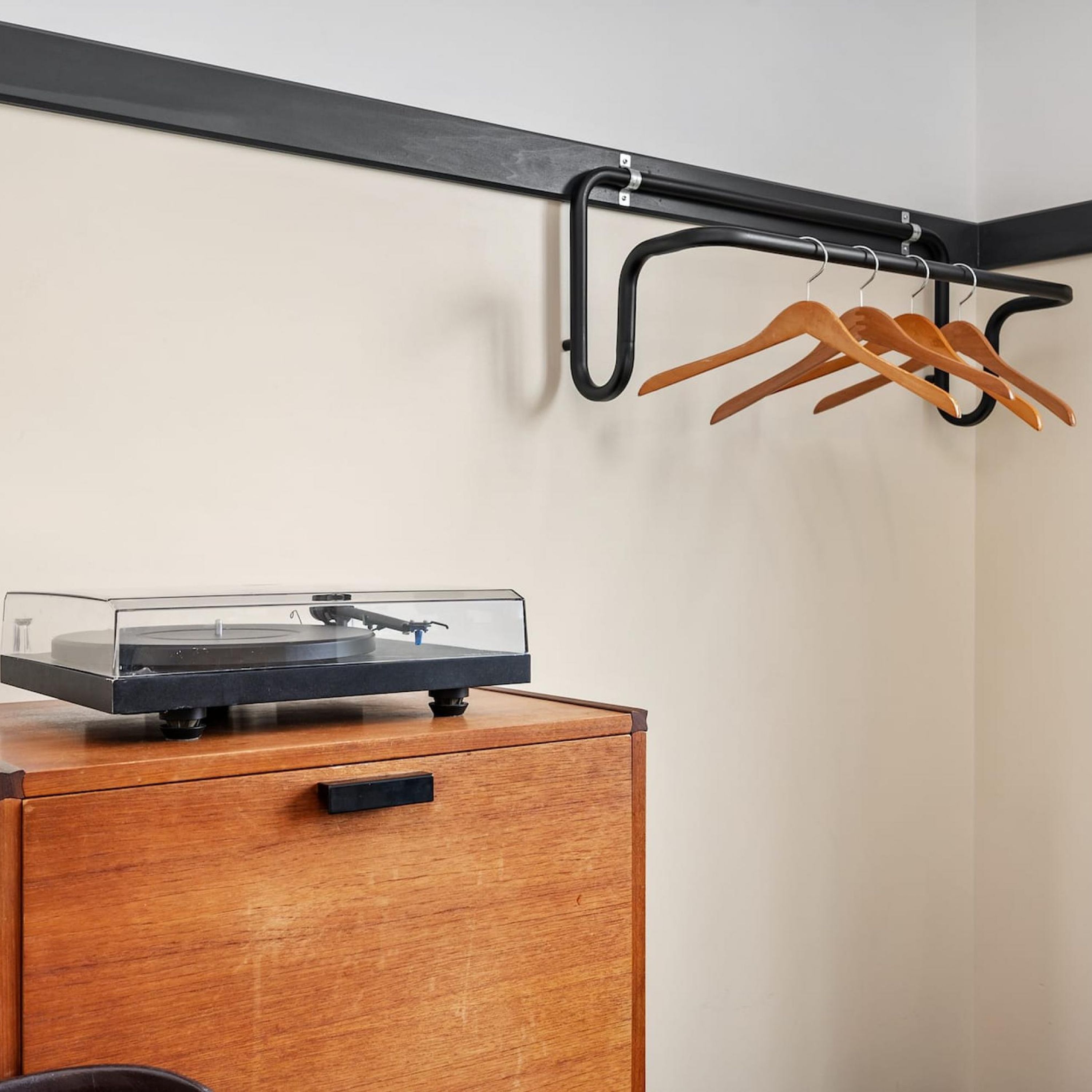 A wooden cabinet with a record player on top, a black metal rack with wooden hangers, and a white wall.
