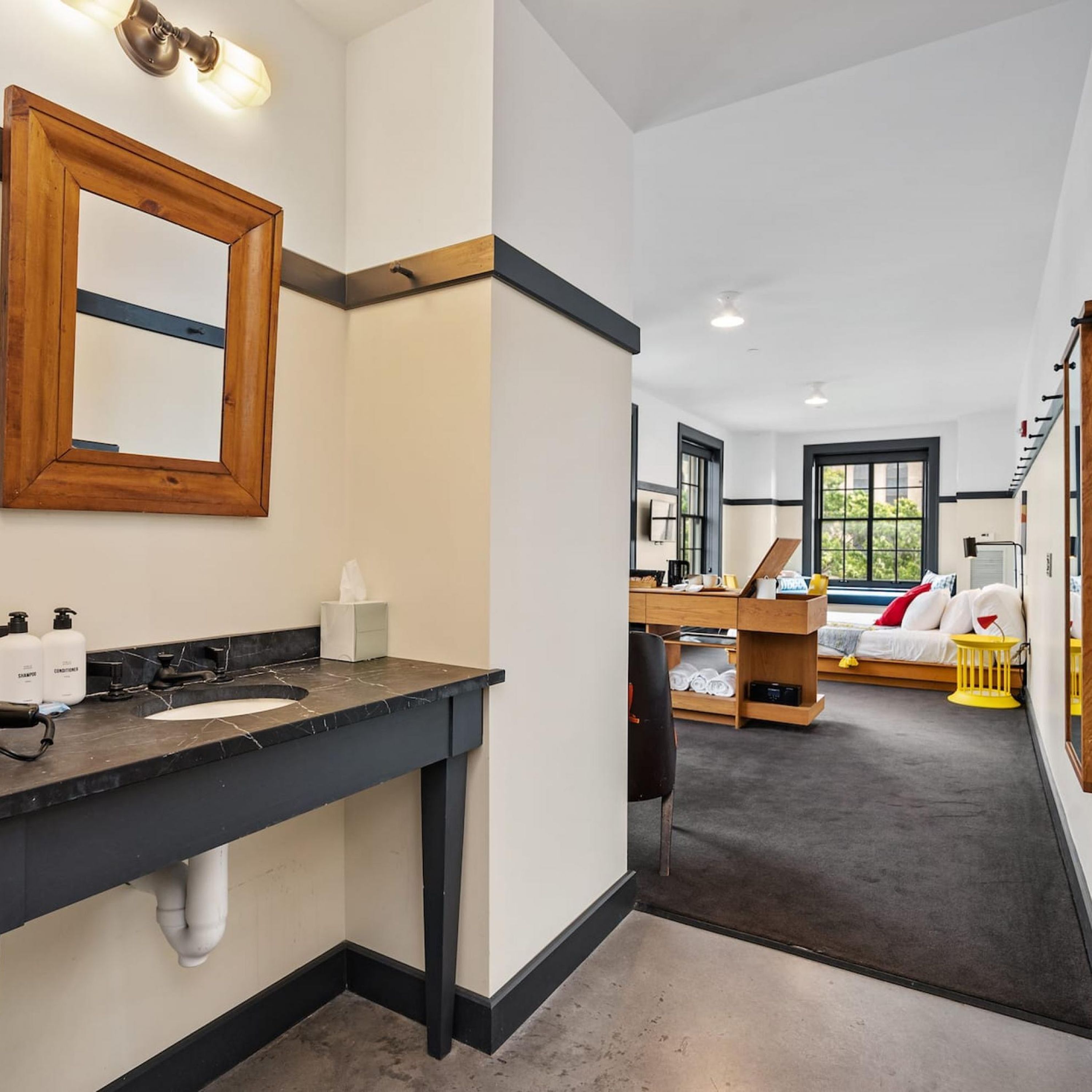 A modern bathroom with a dark countertop, a wooden-framed mirror, and a large window.