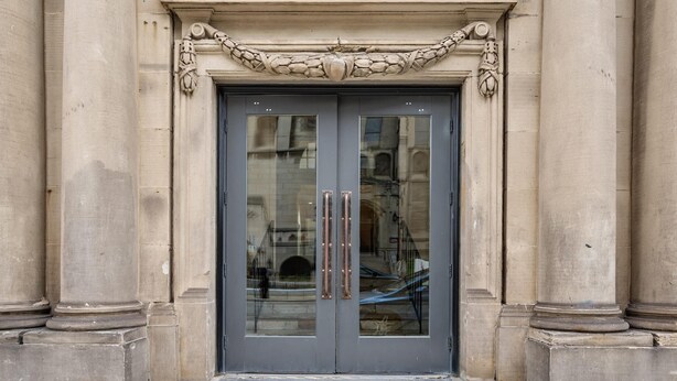 A double door with a reflective glass panel and a decorative stone cornice above.