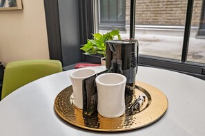 Een tafel met twee witte bekers, een metalen mok, en een dienblad met een plant en een rood voorwerp.