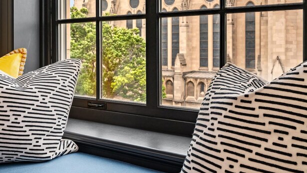 A window seat with patterned cushions, overlooking a historic building with multiple towers and arched windows. - Kasa Classic Studio Inviting Neighborhood Exciting Sights The Maverick (Pittsburgh)