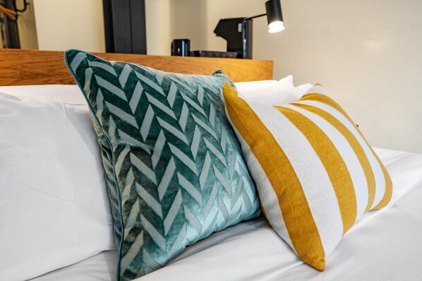 A bed with white sheets, a teal and white chevron pillow, and a mustard and white striped pillow.