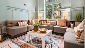 A spacious living room with a large window, a patterned rug, and multiple sofas with decorative pillows.