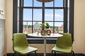 Une pièce dotée d’une grande fenêtre, de deux fauteuils verts, d’une petite table ronde agrémentée d’un objet décoratif, et offrant une vue sur un bâtiment surmonté d’un dôme.