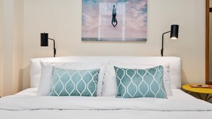 A bed with white linens and two patterned pillows, a painting of a person hanging from a rope, and two black wall lamps. - Kasa Quick Walk to Kelly Strayhorn Theater The Maverick (Pittsburgh)