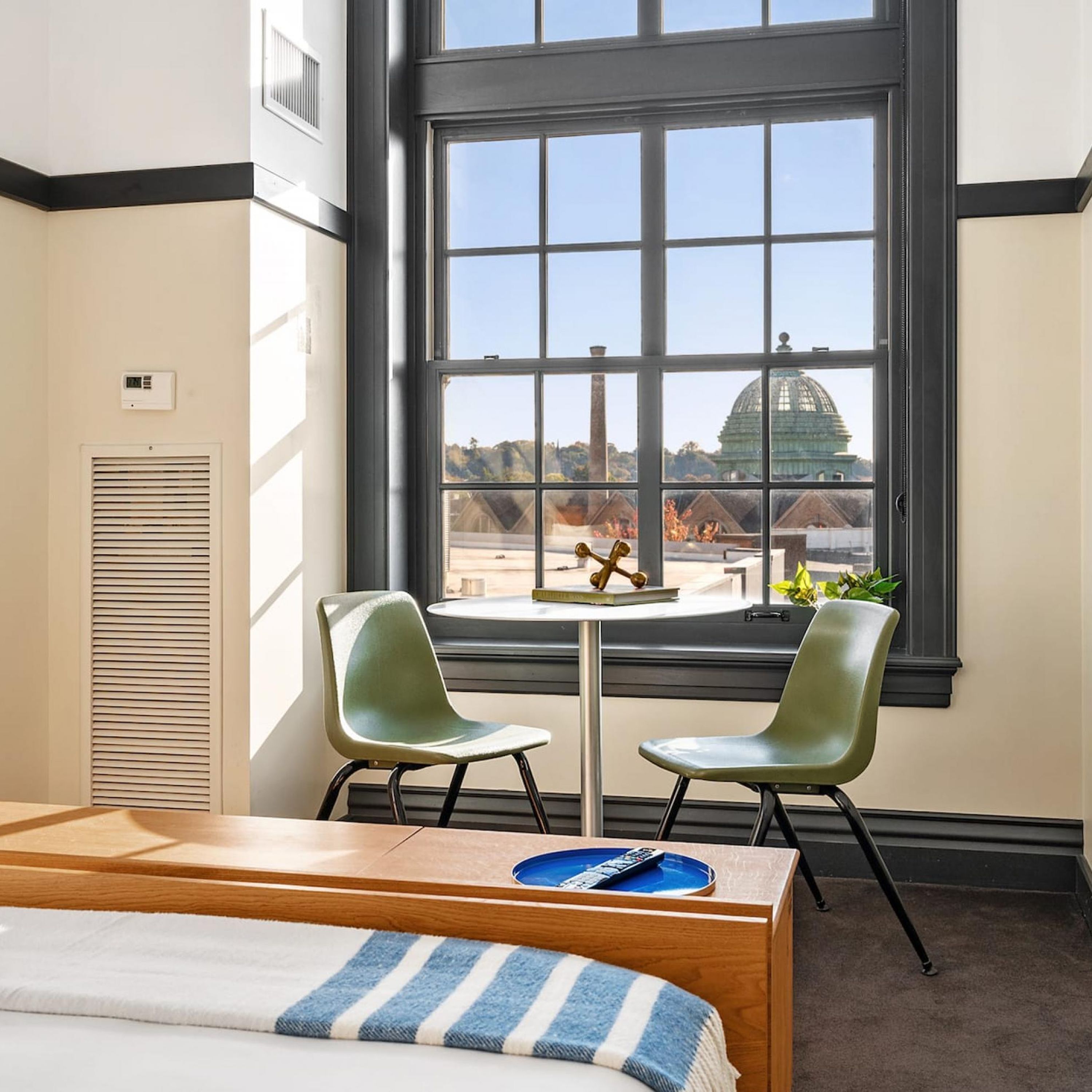 Ein Hotelzimmer mit großem Fenster, zwei Stühlen, einem kleinen Tisch, einem Bett und einer Heizung.