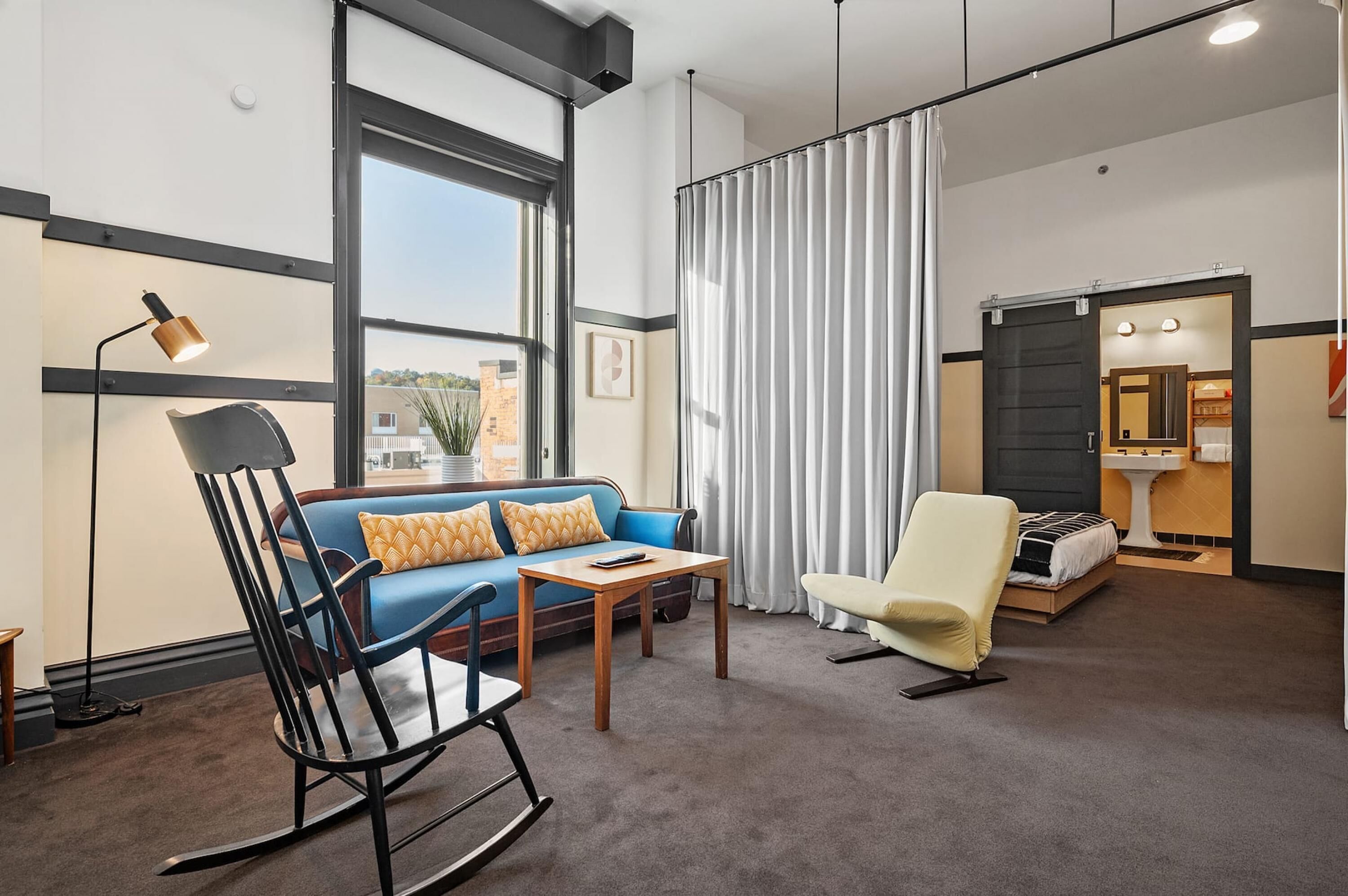 Een moderne hotelkamer met een blauwe bank, een schommelstoel, een bijzettafeltje en een bed.