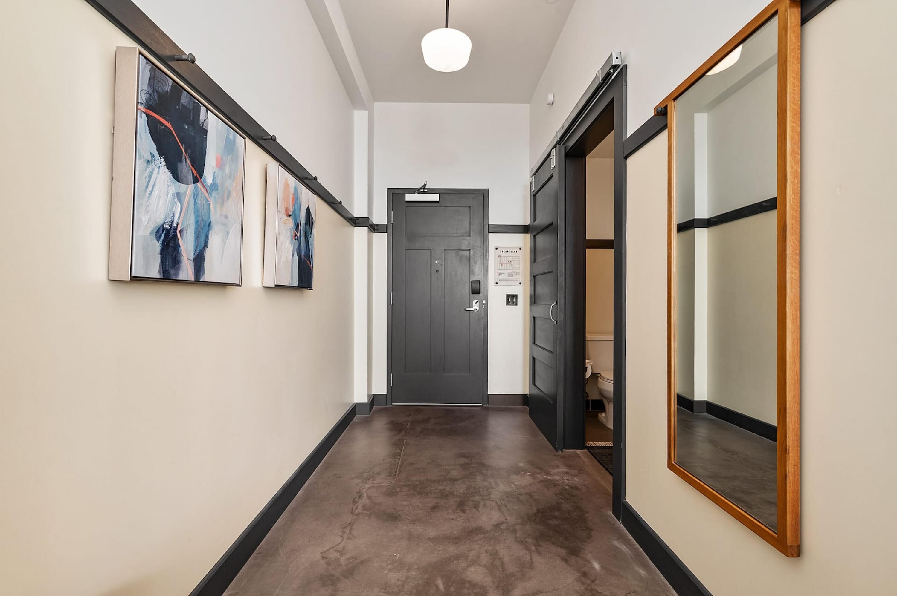 Un pasillo con piso oscuro, una puerta con un letrero y un espejo grande a la derecha.