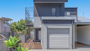 A modern two-story house with a garage, a balcony, and a wooden deck. - Wake up each morning just steps away from 7-mile Beach and the iconic boardwalk (Lennox Head)