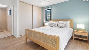 A bedroom with a wooden bed, a nightstand with a lamp, a ceiling fan, and a window with curtains. - Wake up each morning just steps away from 7-mile Beach and the iconic boardwalk (Lennox Head)