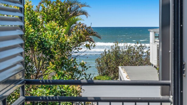 A view of the ocean from a balcony with a railing, surrounded by greenery. - Wake up each morning just steps away from 7-mile Beach and the iconic boardwalk (Lennox Head)