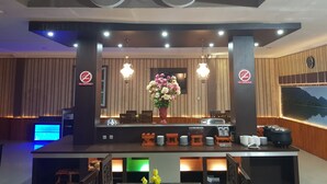 Een hotel receptie met een balie, 'Niet roken'-borden, een bloemstuk en een klok aan de muur.