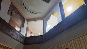Een meerlaags interieur met een decoratief plafond, behang met een patroon en een ingelijste schilderij.