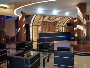 A hotel lobby with a reception desk, seating area, and decorative wall panels. - Capital O 93263 Linge Land Hotel (Takengon)