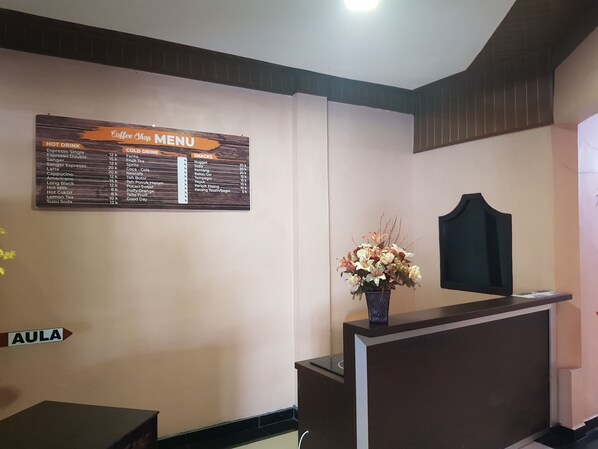 A reception area with a coffee shop menu, a reception desk, and a directional sign labeled "AULA". - Capital O 93263 Linge Land Hotel (Takengon)