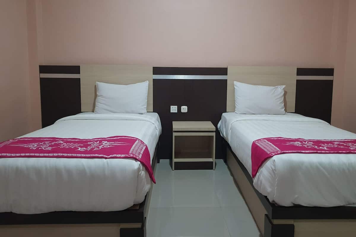 Ein Hotelzimmer mit zwei Einzelbetten, jeweils mit weißer Bettdecke und einer pinkfarbenen Zierdecke. Zwischen den Betten befindet sich ein kleiner Nachttisch, und die Wände sind in einem hellen Pfirsichfarbton gestrichen.